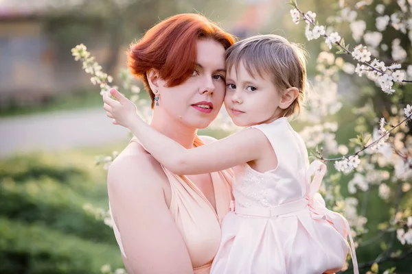 Mamá con una hija al lado de un manzano en flor mira a la cámara — Foto de Stock