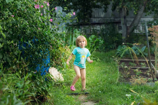 Niña en una camiseta azul hace caras en el jardín . — Foto de Stock