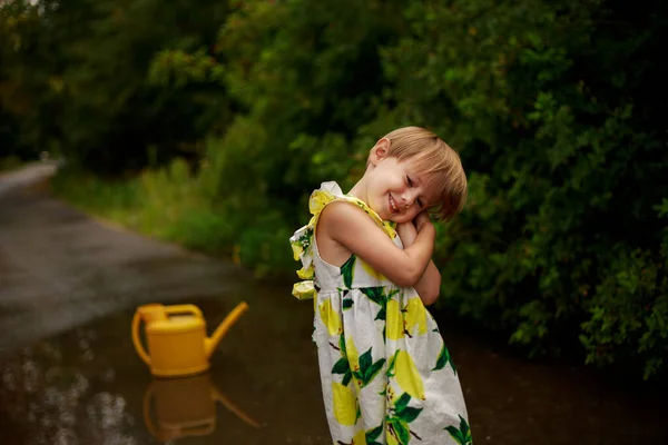 Pequena menina loira em um vestido colorido com uma lata de rega amarela sorrindo — Fotografia de Stock