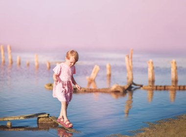 Yaşlı bir kız sahilde karaya oturmuş çürümüş kütüğün üzerinde dikiliyor.