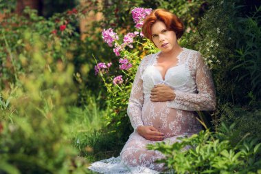 Bahçede dinlenen, gülümseyen 30 yaşında hamile bir kadın. Açık havada poz vermek. 