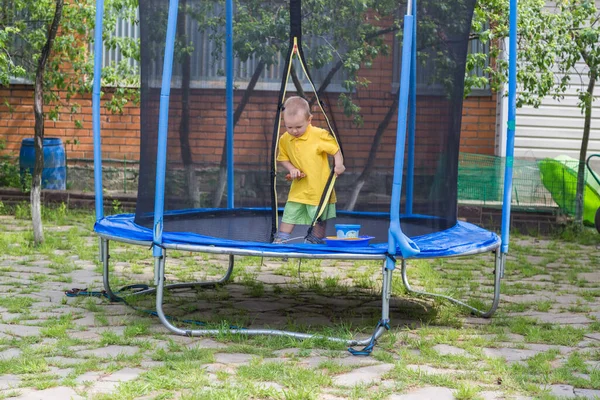 Um menino em uma camiseta amarela pula em um grande trampolim no jardim — Fotografia de Stock