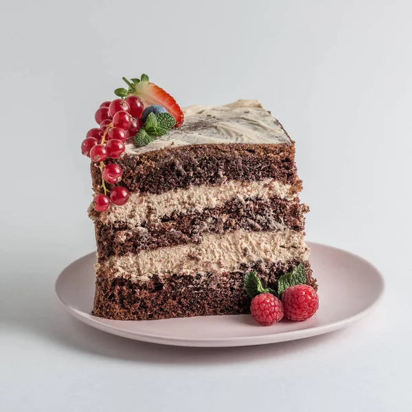 Slice of chocolate sponge cake on a white plate with cream and berries side view — Stock Photo, Image