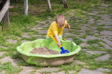 Küçük bir çocuk bahçedeki kum havuzunda oynuyor.