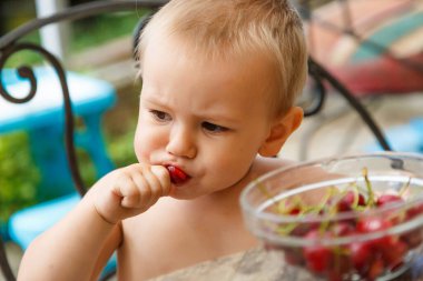 Bahçede kiraz yiyen tatlı, mutlu çocuk.