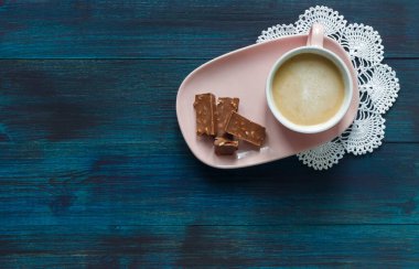 Pembe bir fincan kahve, pembe bir tabakta, beyaz bir peçetenin üzerinde. 