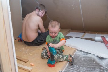 Küçük çocuk bir tornavida tutuyor ve babasına yardım ediyor.