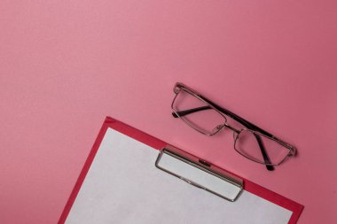 Dizin içindeki gözlük ve kağıt pembe arkaplanda izole bir şekilde duruyor