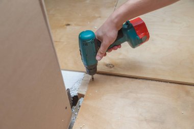 El bir tornavida tutuyor ve vidayı kontrplak levhaya vidalıyor..