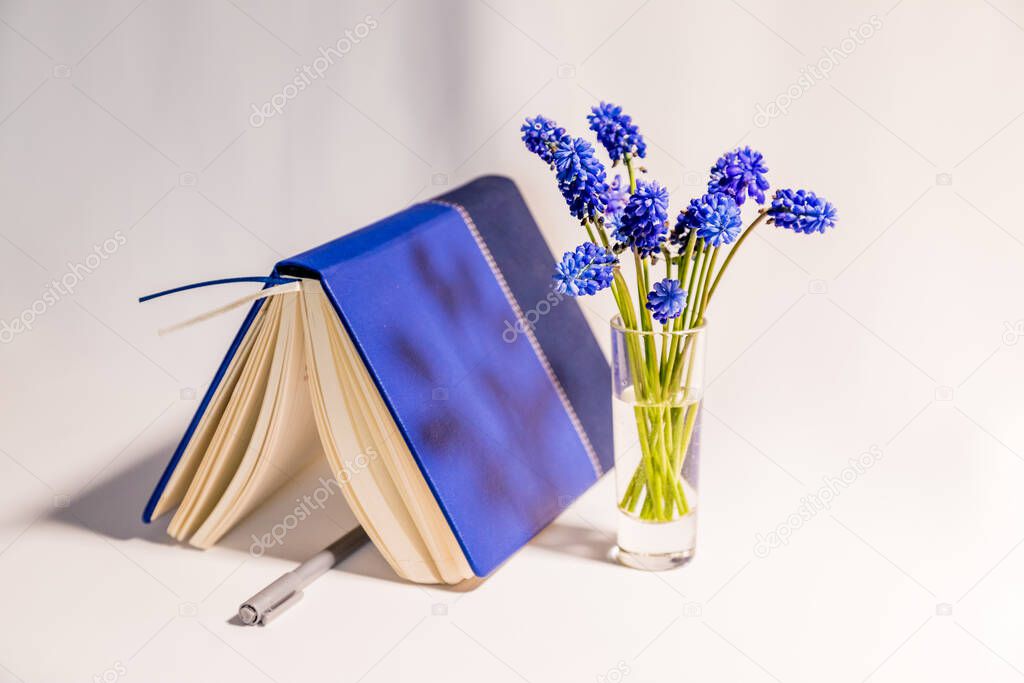 Blue flowers are on the white table and diary with pen top view