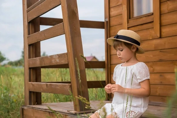 Niña en un vestido boho blanco y un sombrero sobre el fondo de una casa . —  Fotos de Stock