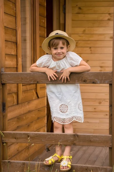 Niña en un vestido boho blanco y un sombrero sobre el fondo de una casa . — Foto de Stock