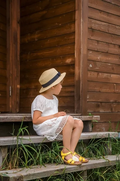 Niña en un vestido boho blanco y un sombrero sobre el fondo de una casa . — Foto de Stock