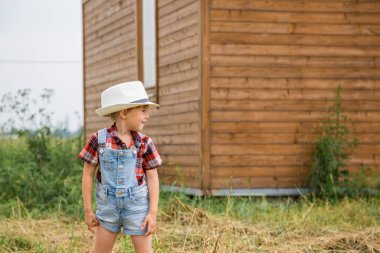 Kot şort ve kırmızı beyaz gömlek giymiş, kovboy şapkalı şirin küçük kız. 