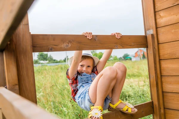 Förtjusande barn flicka, unge cowgirl klättra en veranda av ett trähus. — Stockfoto