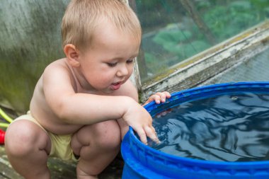 Bir çocuk bahçedeki su varilinde suyla oynuyor..
