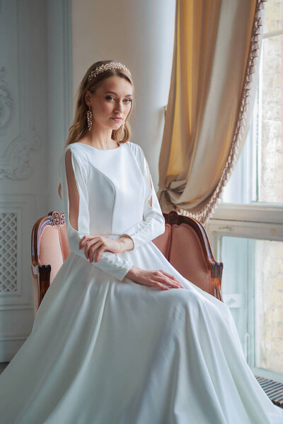 A bride with hairstyle and make up in gougeous wedding dress preparing for the wedding. A portrait of beautiful girl with blond hair and blue eyes in studio