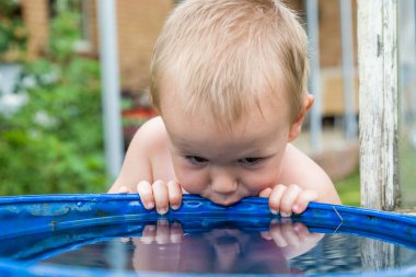 Bir çocuk su varilinden su içmeye çalışıyor..