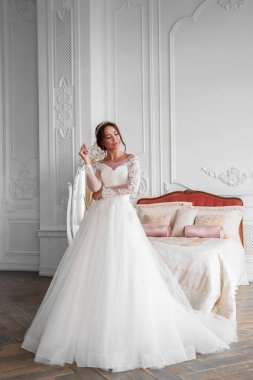 Bir ışık stüdyosunda gelinin tam boy portresi, kız düşünceli bir şekilde yana bakıyor, düğün makyajı ve tasarımı var, pencereden gelen ışık..