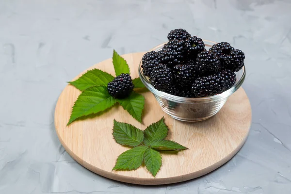 Ripe Blackberries Leaves Glass Bowl Bamboo Cutting Board Concrete Background — Stock Photo, Image