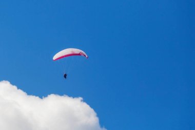 Bir paraglider bulutların arka planında mavi gökyüzünde uçuyor. Güneşli bir günde gökyüzünde paraşütle atlamak.