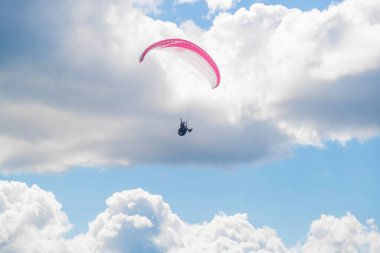 Bir paraglider bulutların arka planında mavi gökyüzünde uçuyor. Güneşli bir günde gökyüzünde paraşütle atlamak.