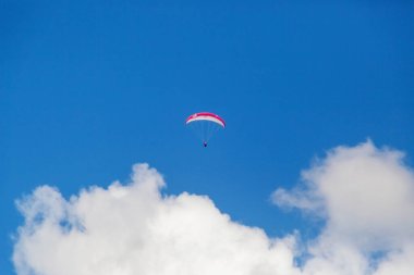 Bir paraglider bulutların arka planında mavi gökyüzünde uçuyor. Güneşli bir günde gökyüzünde paraşütle atlamak.