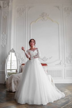 Gelin saç stili esmer bir gelinin portresi düşük açıdan çekilir. Gelin beyaz bir resmi elbise giydi. Fotoğraf bir ışık stüdyosunda çekildi..