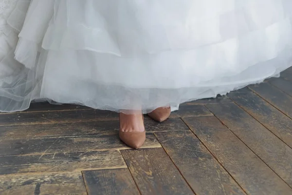 Bride\'s feet in old non-wedding shoes. I forgot to change my shoes. The hem of the dress is raised. The old shabby floor is visible.