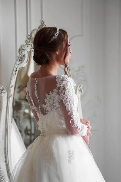 .Portrait of a brunette bride with wedding hairstyle from the back. The bride is dressed in a white formal dress. The photo was taken in a light studio.