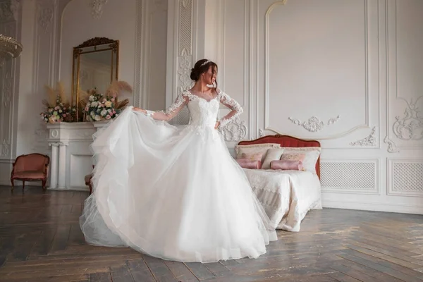 .Beyaz bir elbise içinde esmer bir gelinin portresi. Gelin ne kadar muhteşem bir elbisesi olduğunu gösteriyor, eteği eliyle tutuyor. Fotoğraf bir ışık stüdyosunda çekildi..