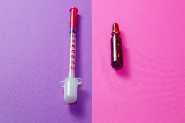 Injectable medications in sealed vials and a disposable plastic medical syringe, soft focus, pink and violet background