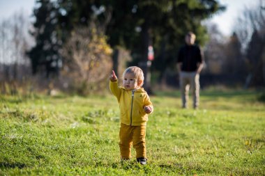 Sarı ceketli bir çocuk parmağını bir sonbahar parkında Hindistan yazında bir şeye doğrultuyor..