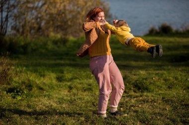 .Anne, sarı ceketli, küçük bir çocuğun kollarıyla sarılıyor onu. Altın sonbahar Hindistan yazı.