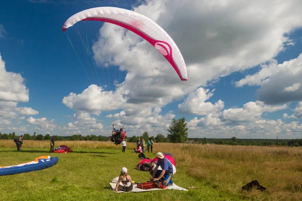 Tver, Rusya - 9 Ağustos 2020: Arka planda bulutlu mavi gökyüzü uçuşundan sonra paraşütle inmek görülüyor. Uçuşları seyreden insanlar.