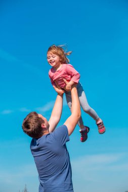 Babalar Günü. Babası kızını açık mavi gökyüzünün arka planına fırlatıyor, yaz tatili mutlu aile kavramı..