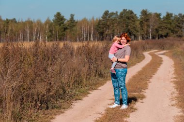 Anneler Günü. Anne kızını kurak çimenler ve kır çiçekleriyle yaz tarlasında kollarında taşıyor. Yaz tatili mutlu aile kavramı.
