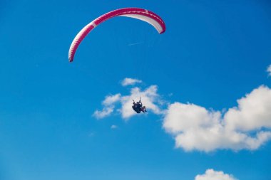 Bir tandem paraglider bulutların arka planında mavi gökyüzünde uçuyor. Güneşli bir günde gökyüzünde paraşütle atlamak.