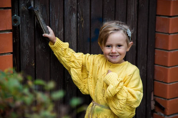 Beautiful happy girl with a short haircut in a yellow knitted sweater is.standing near the fence on a background of red leaves of wild grapes, Welcome warm autumn. Golden autumn concept, Indian summer