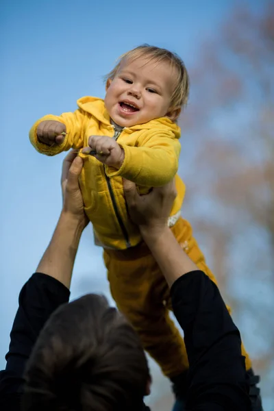 Apa Feldob Egy Babát Sárga Kabátban Levegőbe Gyerek Nevet Jól — Stock Fotó