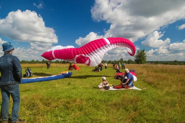 Tver, Rusya - 9 Ağustos 2020: Arka planda bulutlu mavi gökyüzü uçuşundan sonra paraşütle inmek görülüyor. Uçuşları seyreden insanlar.