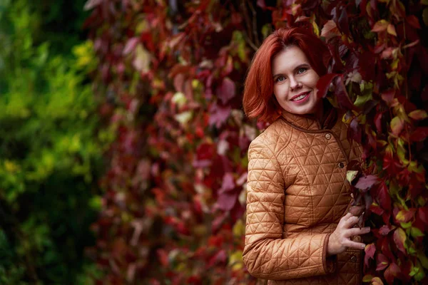 Genç ve güzel bir kadın kırmızı yapraklarla kaplı bir üzüm çitinin yanında duruyor. Altın sonbahar, Hint Yazı.