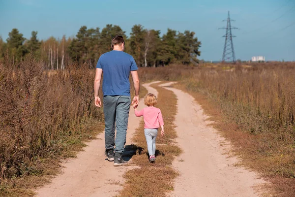 .Vista trasera del padre cogido de la mano con su hija y caminando en el campo — Foto de Stock