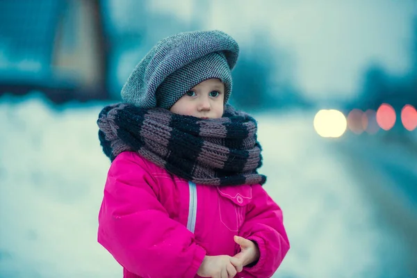 .Ein kleines Mädchen steht abends am Straßenrand im Schnee — Stockfoto