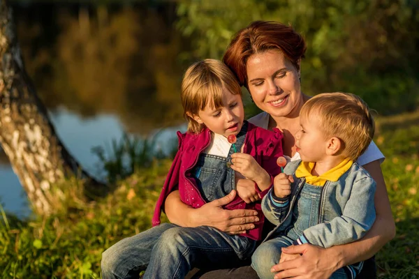 Familia feliz mamá y los niños se sientan en la orilla del río — Foto de Stock