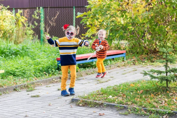 Una niña con la cara pintada, huyendo de su hermano en el patio de recreo — Foto de Stock