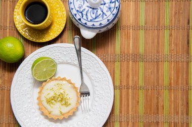 Çeşitli mutfak aksesuarlarının üst görüntüsü. Sarı kahve fincanı, mavi tabakta limonlu turta, kaşık, kesme tahtası, paslanmaz çelik spatula, yazı için boş alanı olan rende. Boşluğu kopyala.