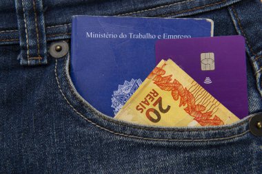 Kotların, kredi kartlarının ve Brezilya banknotlarının ön cebindeki cep telefonunu kapat. Çeviri: Dijital çalışma belgesi (Carteira de trabalho digital).