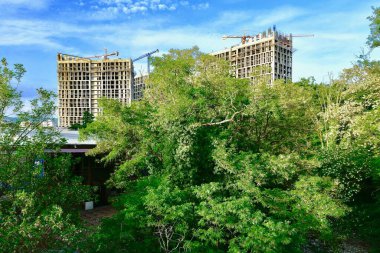 Mavi gökyüzüne karşı çevresi bitki örtüsüyle çevrili iki yüksek bina yapım aşamasında.