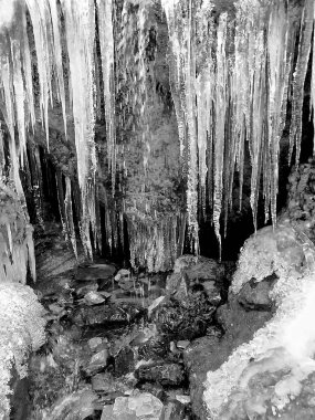 Buz saçakları donmuş bir dağ deresinin üzerinde kümeler halinde asılı, dibi çakıllı ve kıyılar boyunca kar birikiyor.